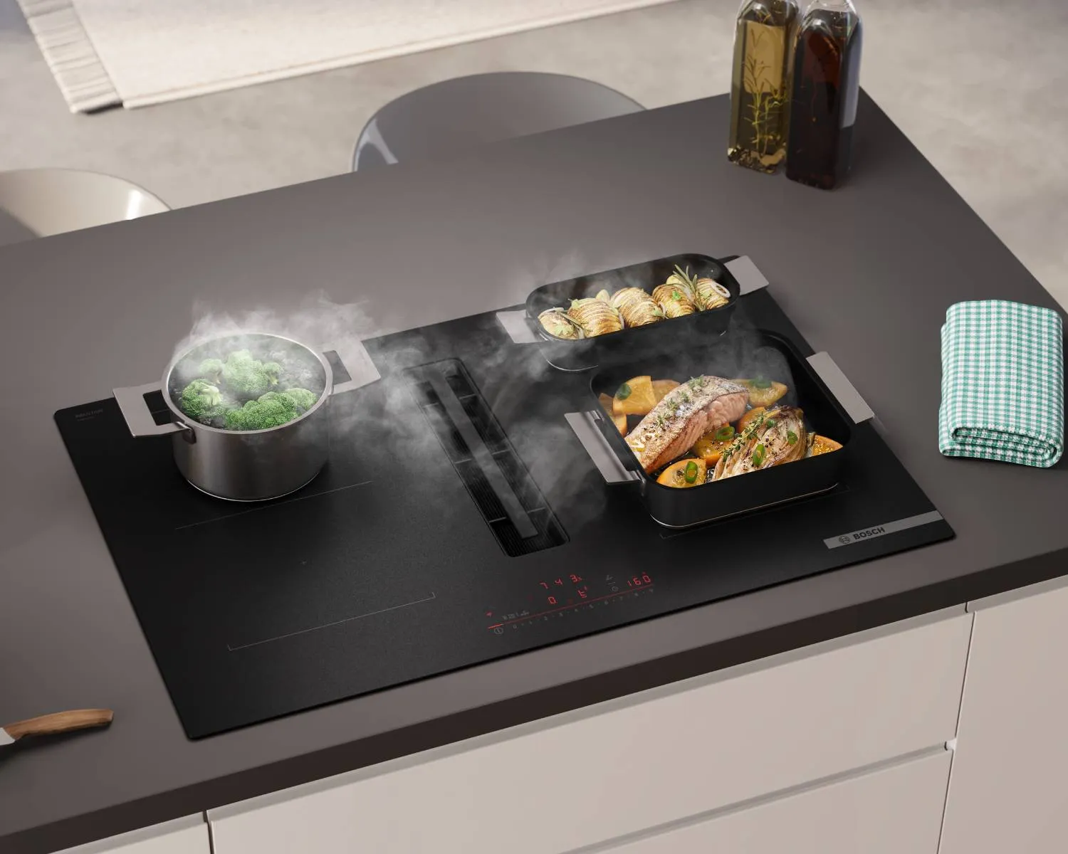A black Bosch induction cooktop with an integrated downdraft extractor, cooking broccoli, salmon with vegetables, and potatoes in steaming pots and pans.