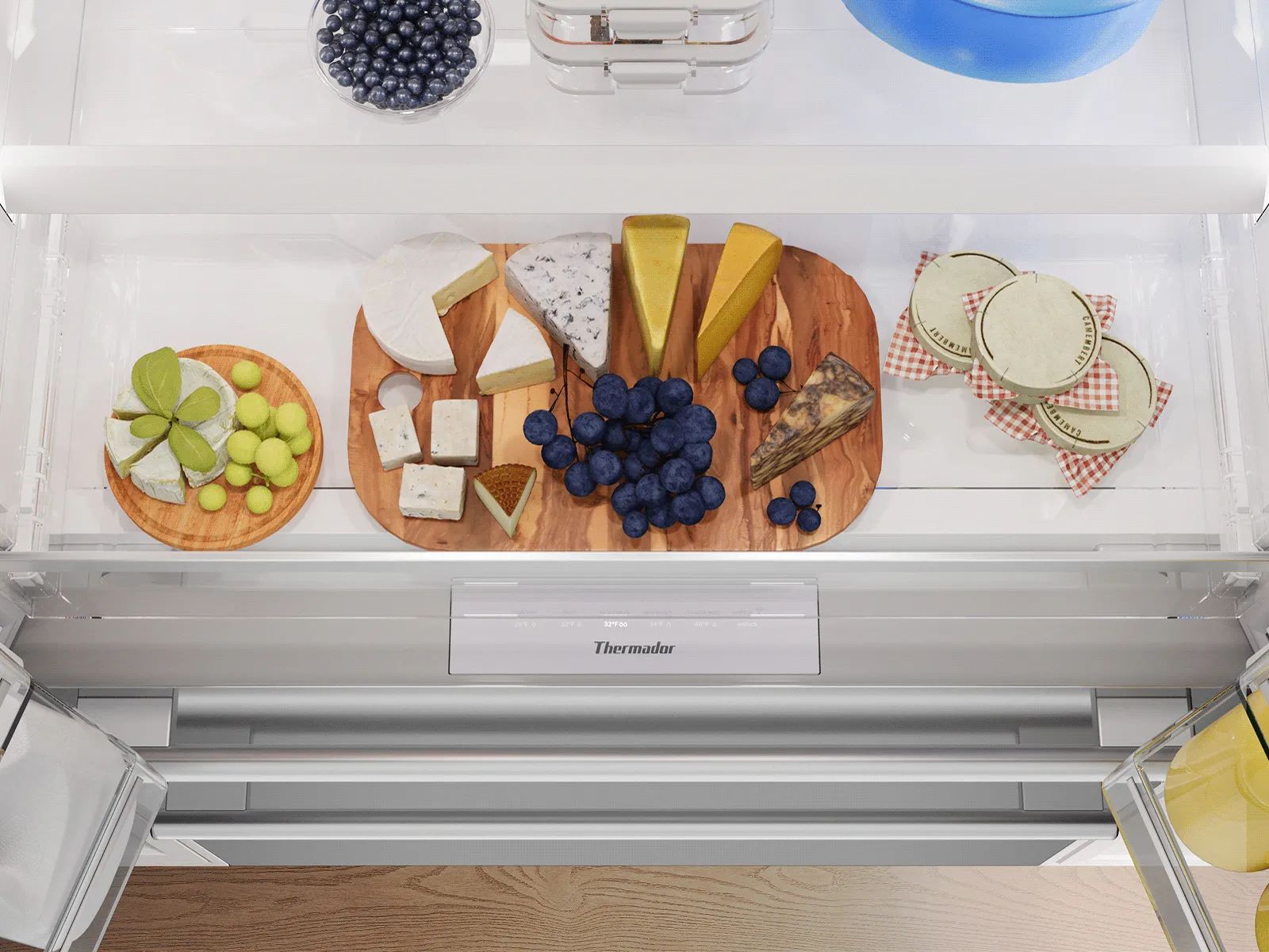 Wide refrigerator drawer displaying assorted cheeses, grapes, and fresh food items