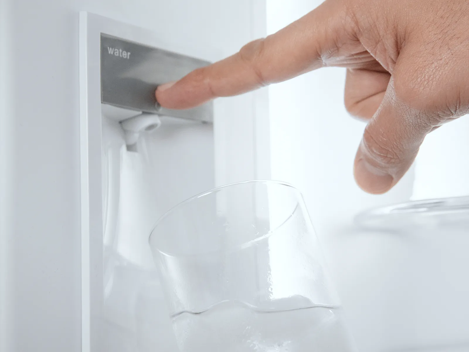 A hand presses a button to dispense filtered water from an internal dispenser into a glass.