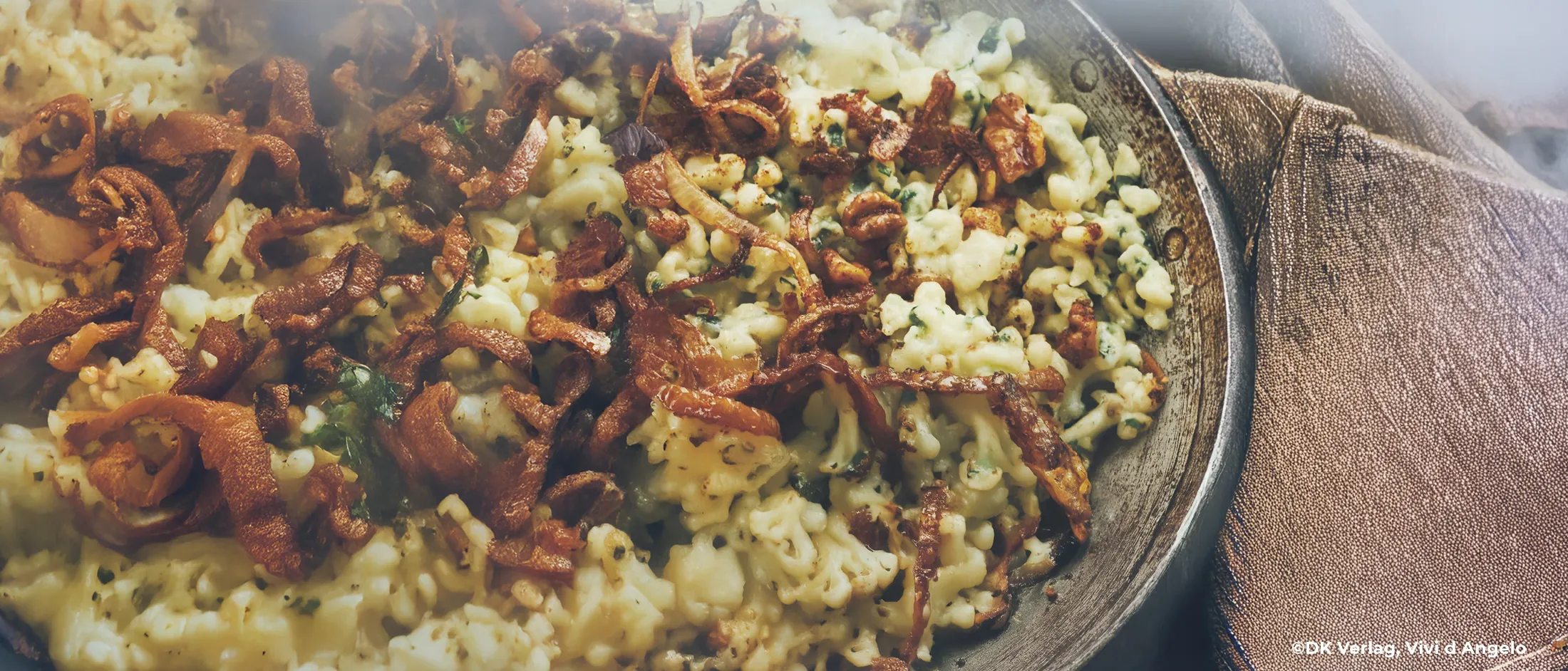 Pfanne mit Spinatspätzle und gebratenen Zwiebeln auf grauem Untergrund