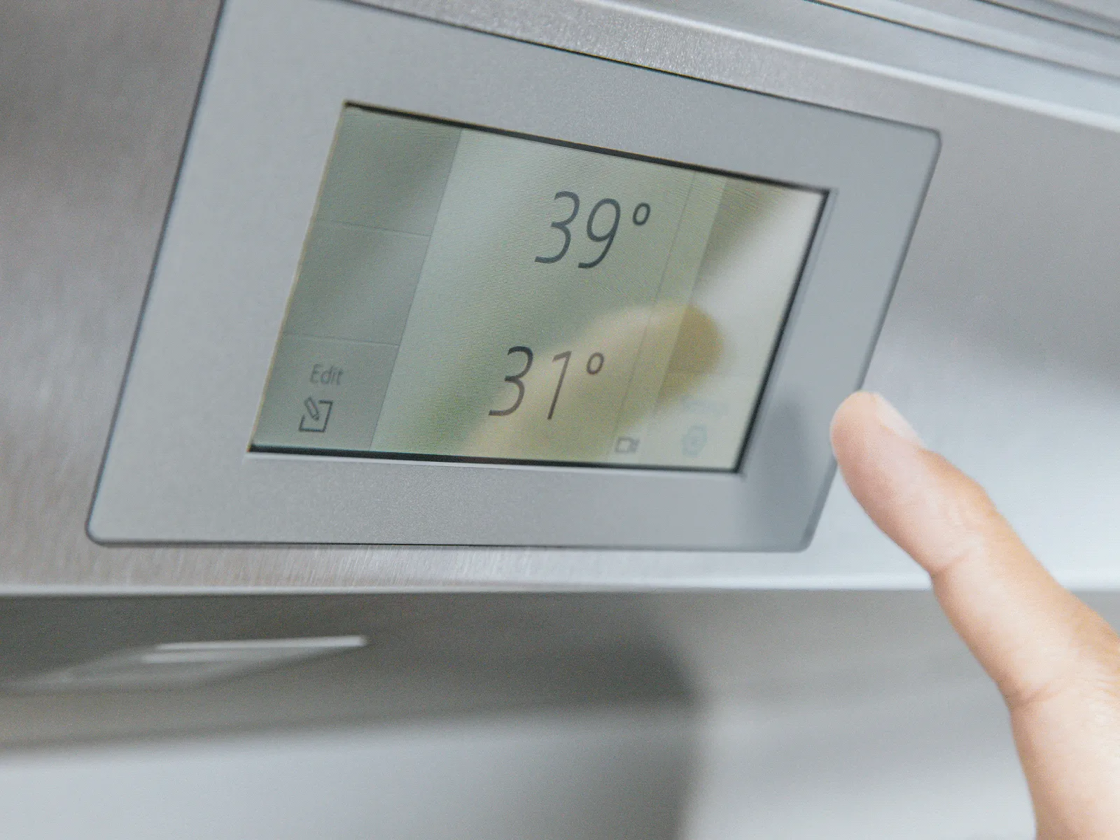 Close-up of a hand adjusting a digital thermostat displaying temperatures of 39° and 31°.