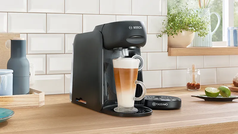 Une machine à café noire posée sur le plan de travail en bois d'une cuisine sert un café.