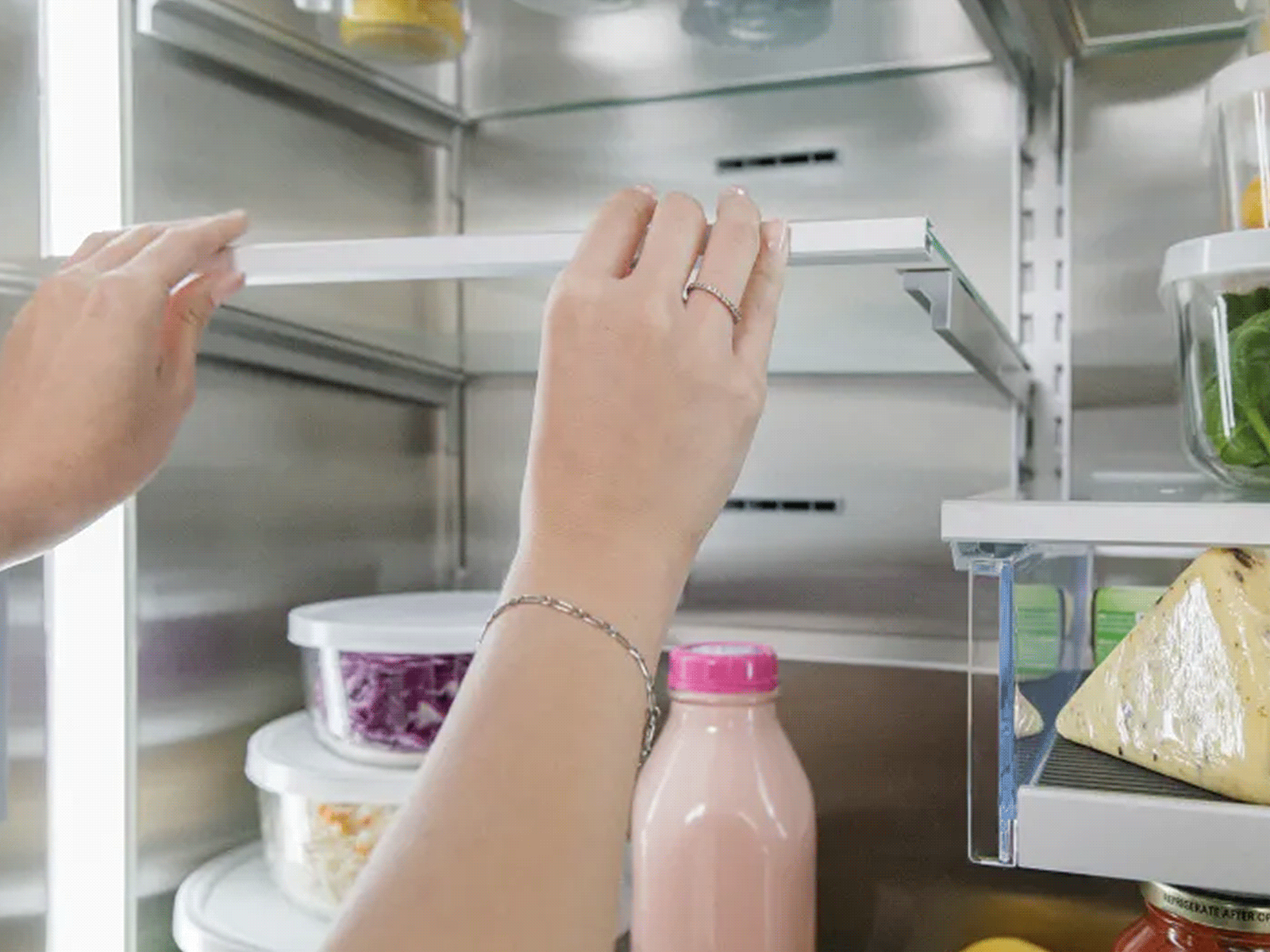 Close-up of hands lifting an adjustable glass refrigerator shelf to change its position.