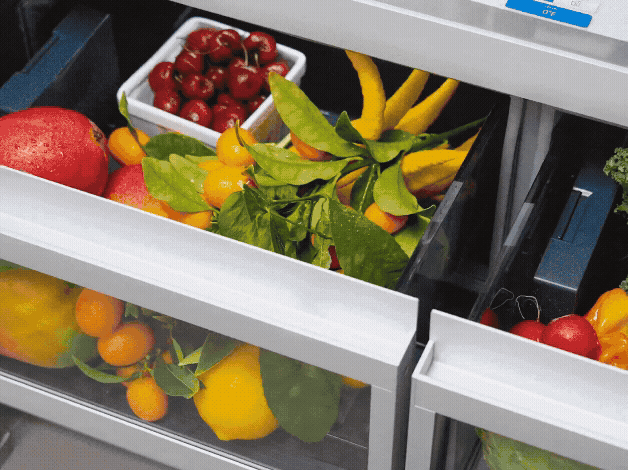 Refrigerator crisper drawers filled with colorful fresh fruits and vegetables.