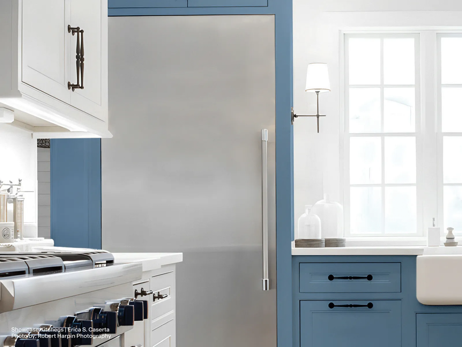 Built-in stainless steel freezer column integrated into blue and white kitchen cabinetry, with adjacent countertop, range, and a window allowing natural light into the space.