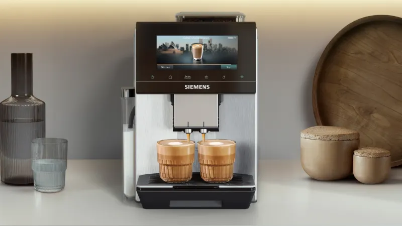 Siemens EQ900 (plus) iAroma fully automatic coffee machine brewing two cappuccinos, surrounded by various coffee specialities.