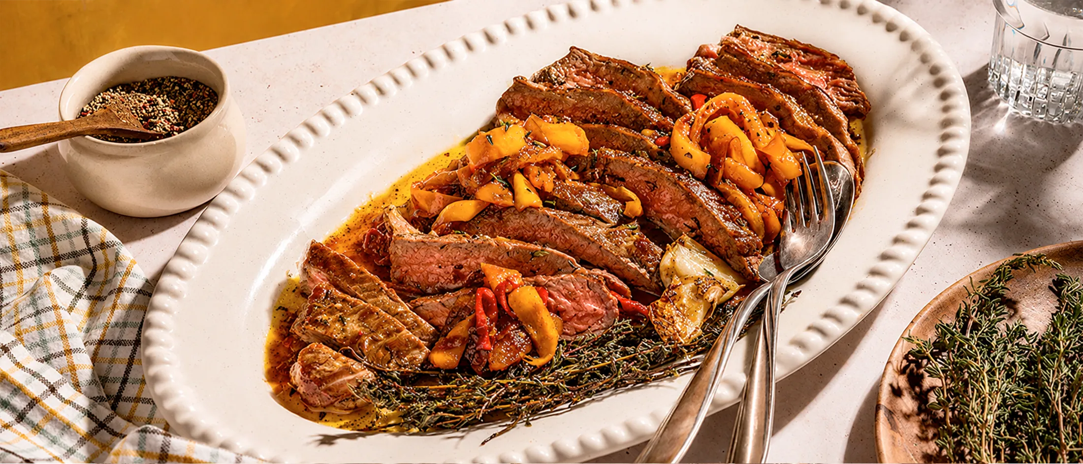 Grilled steak slices with roasted vegetables on a white plate, garnished with herbs.