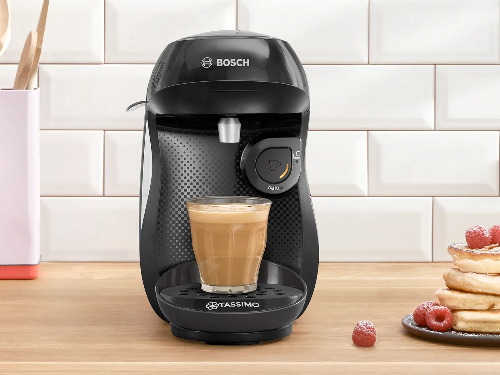 The coffee machine TASSIMO HAPPY friendly on a kitchen worktop with a filled coffee cup.