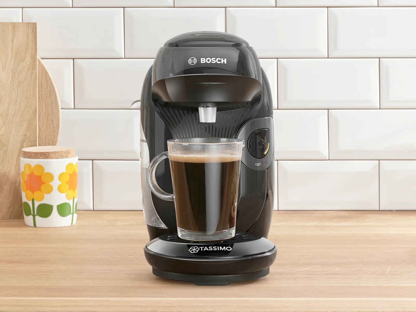 The coffee machine TASSIMO STYLE friendly on a kitchen worktop with a filled coffee cup.