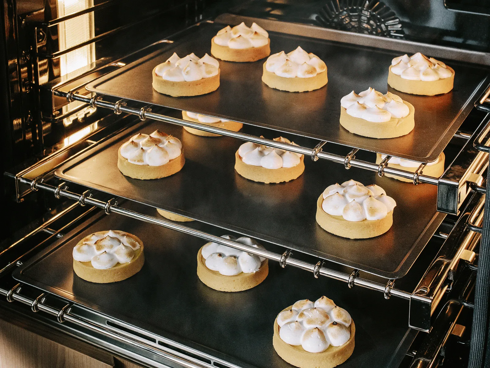 Cookies with meringue topping baking in a three-rack oven, evenly spaced on trays.