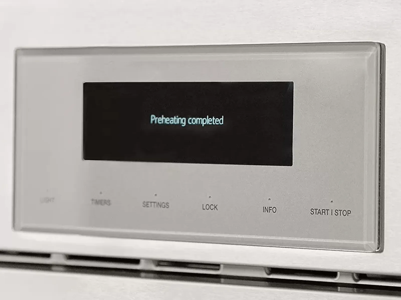 Oven control panel displaying 'Preheating completed,' with buttons for light, timer, and settings.