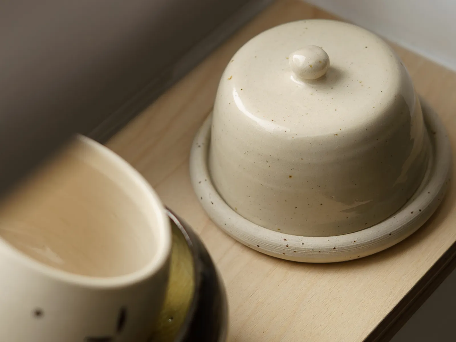 A speckled ceramic butter dish with a domed lid and knob sits on a light wooden shelf.