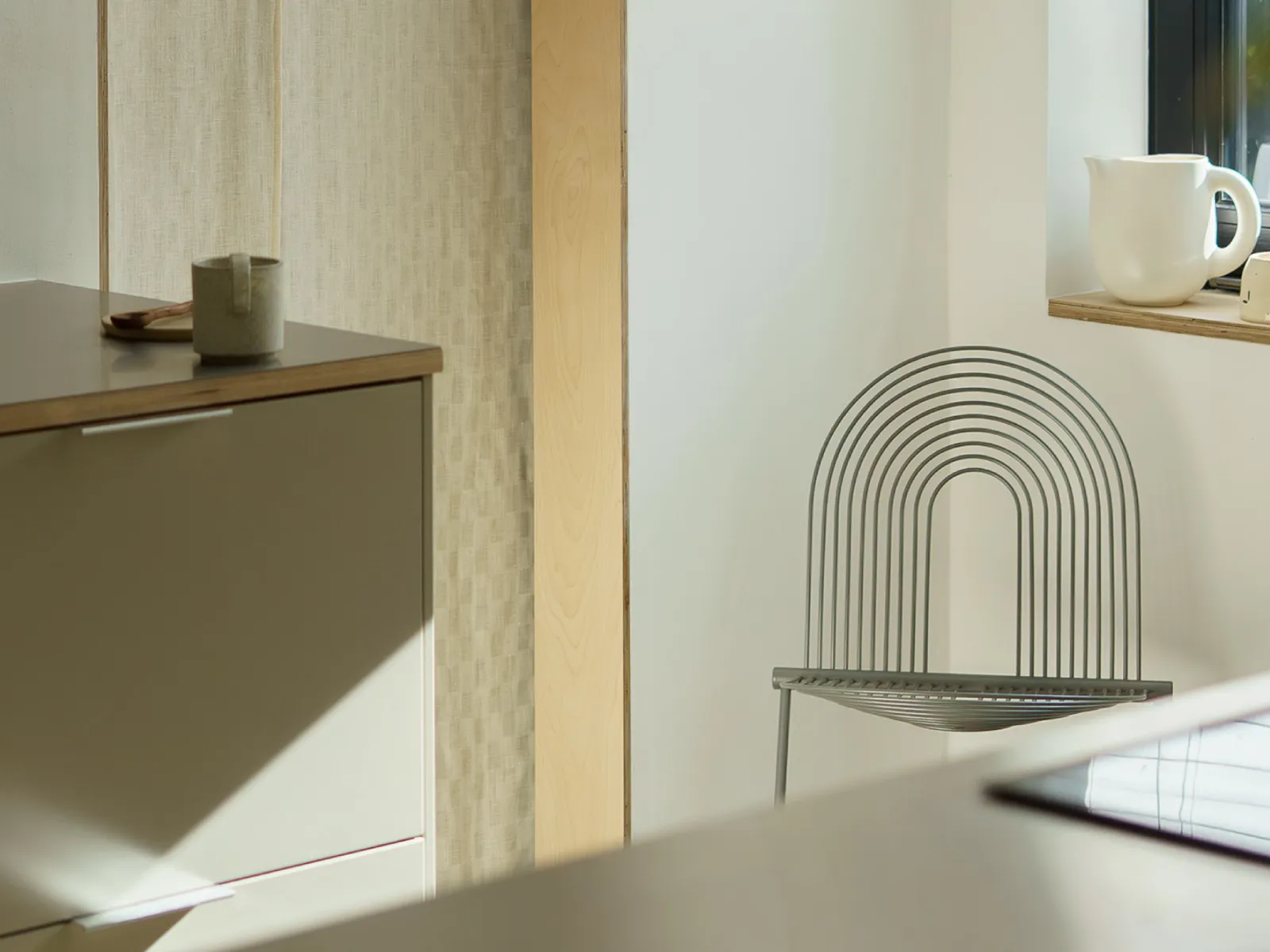 A modern kitchen with light gray cabinets, a wooden cutting board, and a unique metal chair.