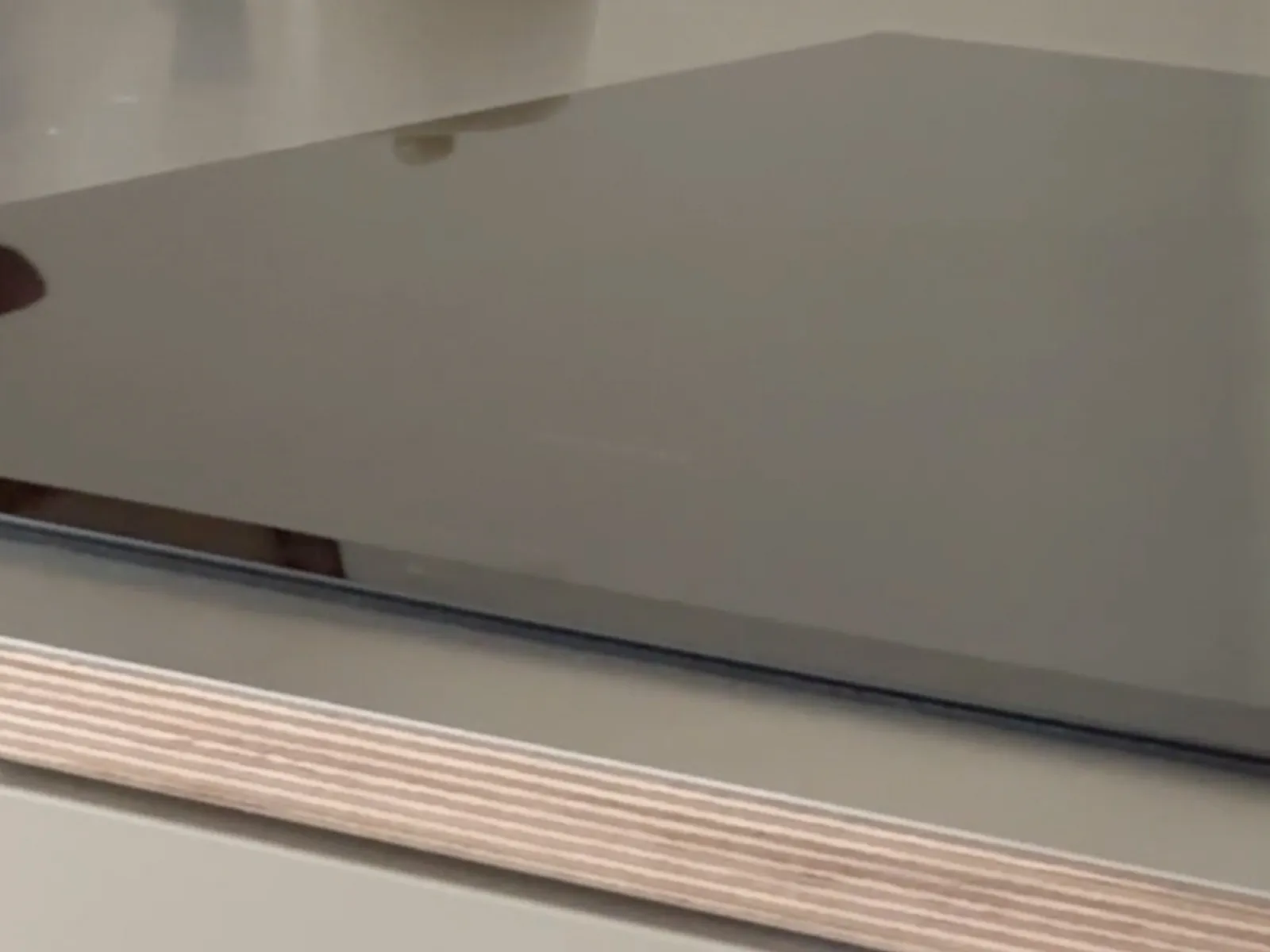 Closed black laptop resting on a light-colored wooden surface with reflections visible on the laptop lid.