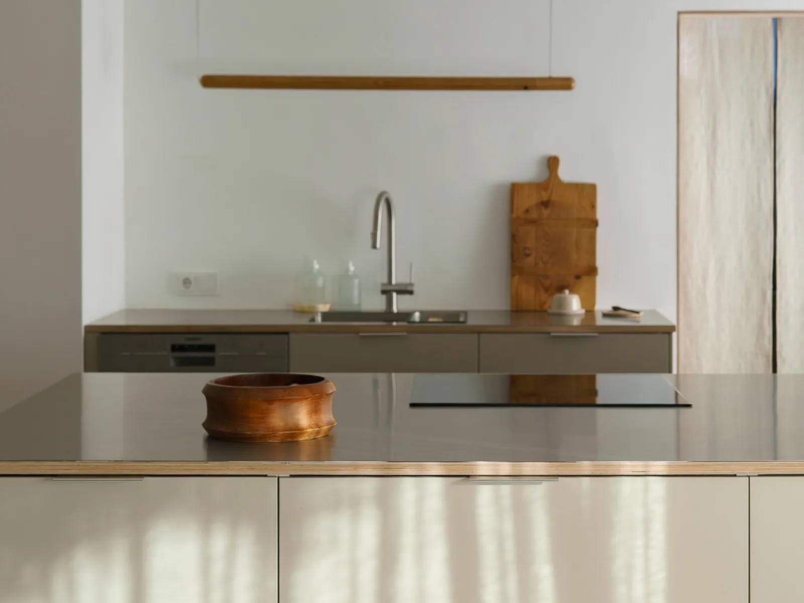 A modern kitchen with light-colored cabinets, a stainless steel countertop, and a wooden bowl in the foreground.