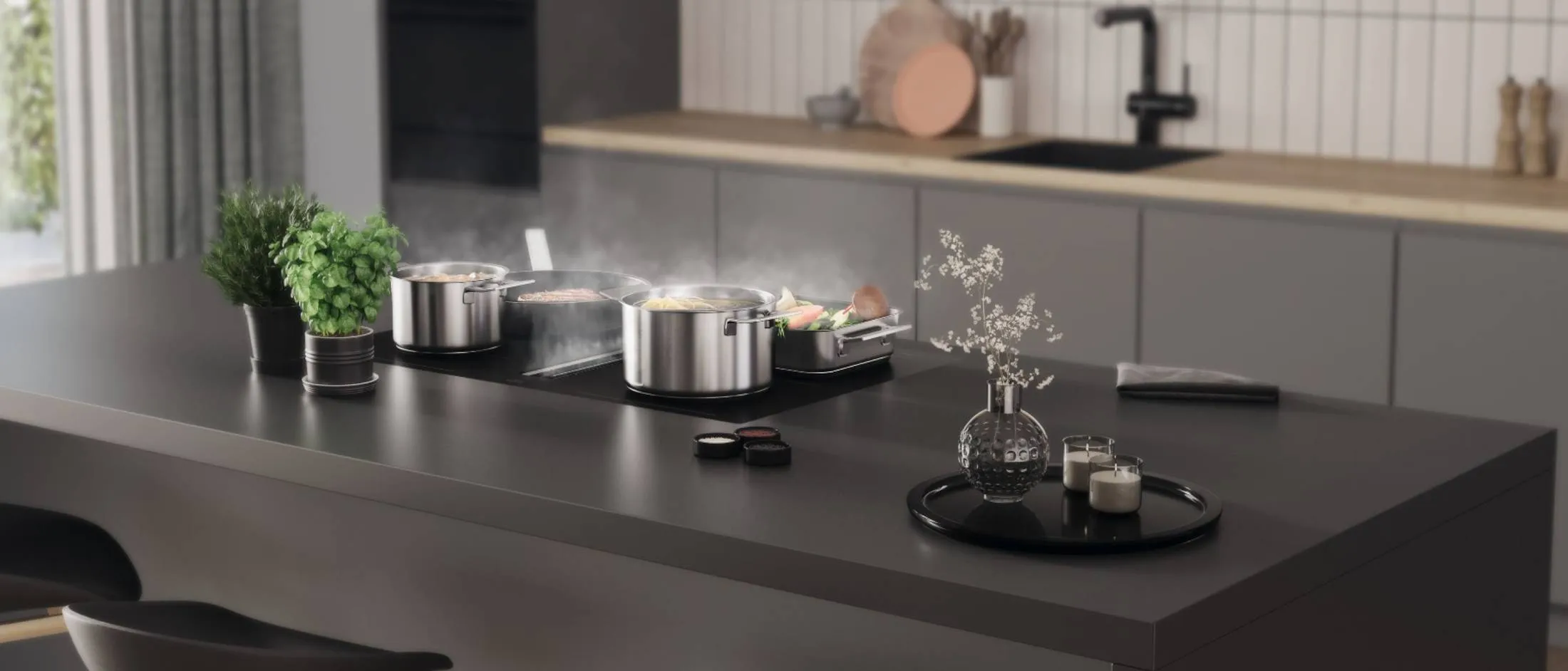 A modern kitchen island with a black induction cooktop, where a pot of pasta, a pan of meat, and a tray of vegetables are steaming, surrounded by fresh herbs and decor.
