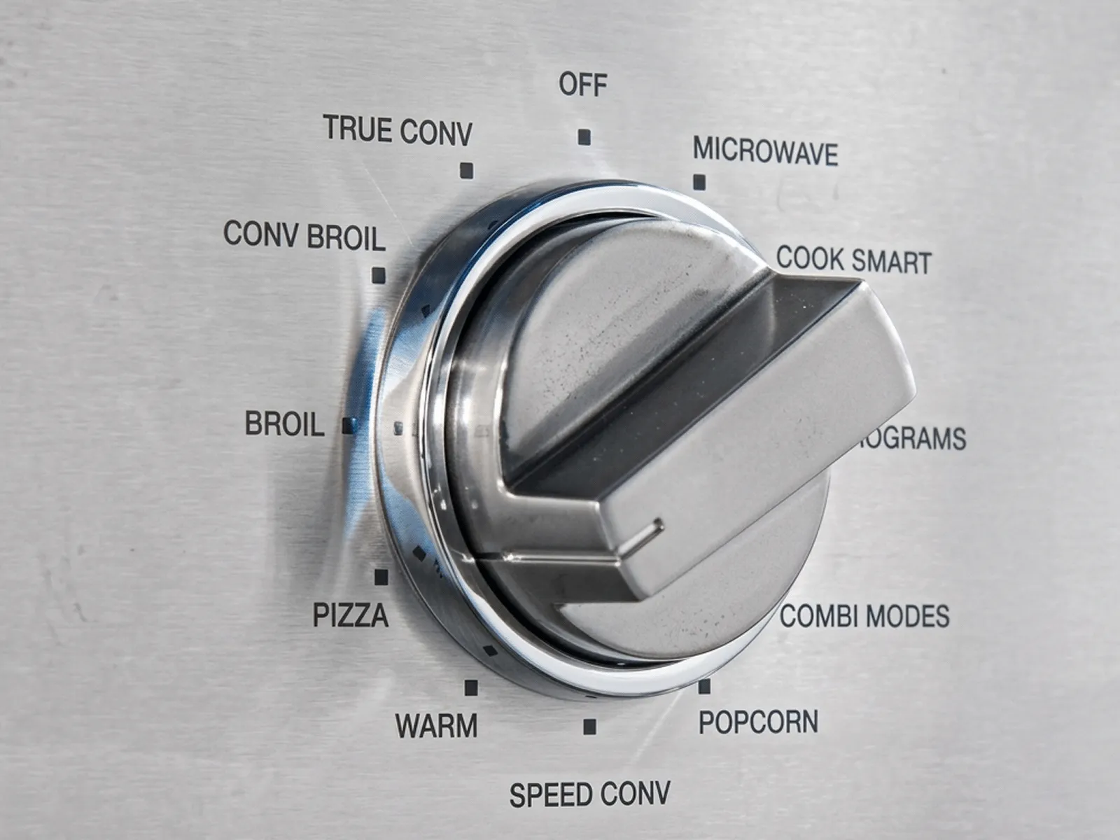 Close-up of a stainless steel oven control knob with various cooking options labeled.