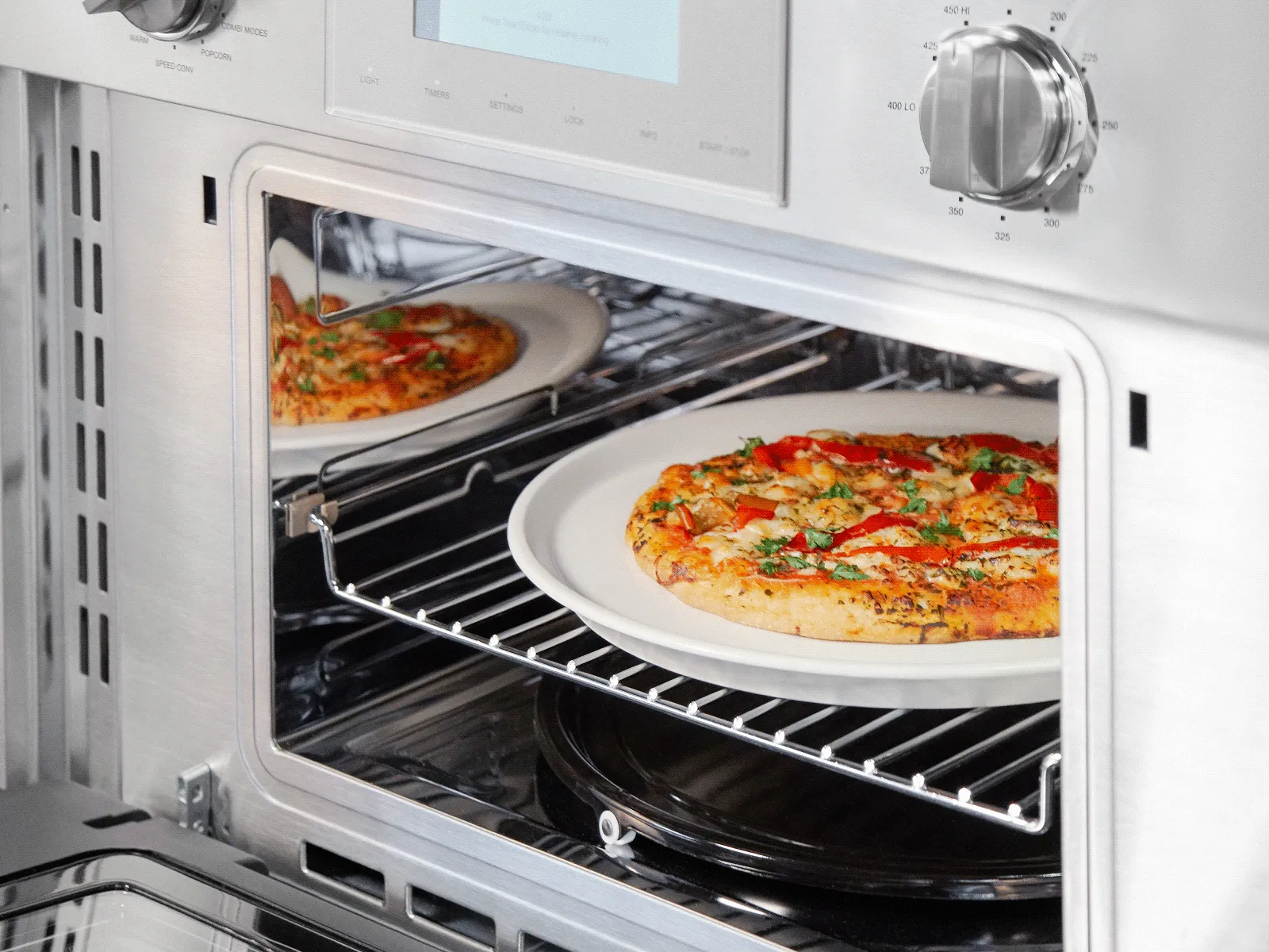 Open oven with a pizza baking inside on a rack, control knobs visible on the top right.