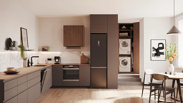 Moderne Küche mit mattbraunen Schränken, Einbaugeräten, Waschmaschine und Trockner, einem Esstisch aus Holz mit Stühlen und minimalistischer Einrichtung.
