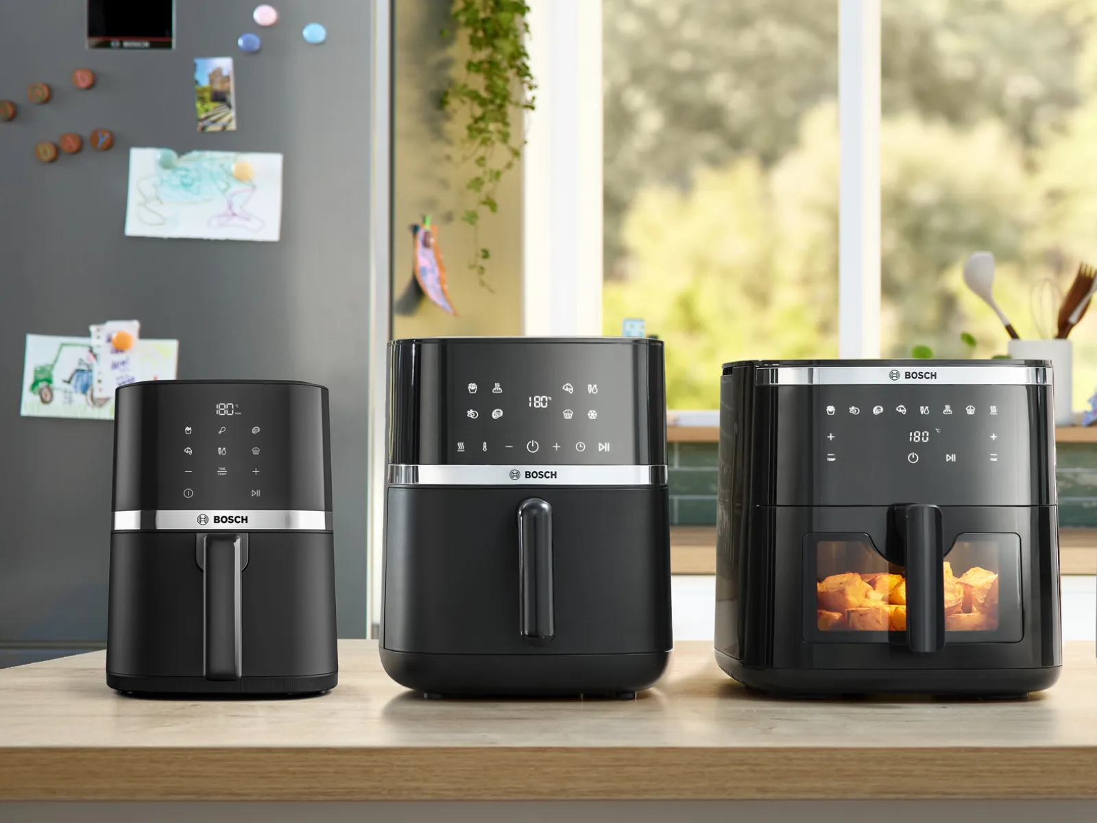 Three Bosch single drawer air fryers stand on a kitchen counter with various dishes next to it.