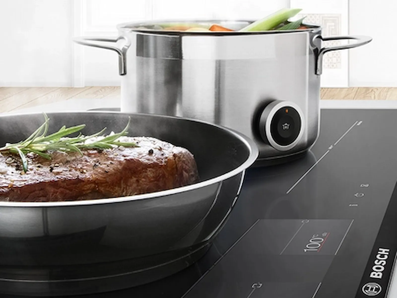 Elegantní indukční varná deska Bosch s pánví se spalujícím steakem a hrncem zeleniny, která představuje moderní technologii vaření.