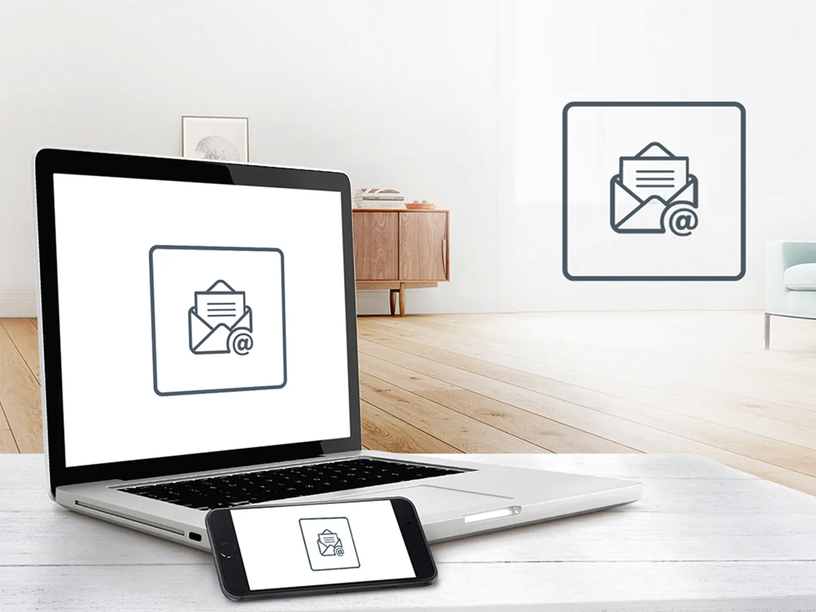 Laptop und Smartphone mit E‑Mail-Symbol vor hellem Wohnzimmer.