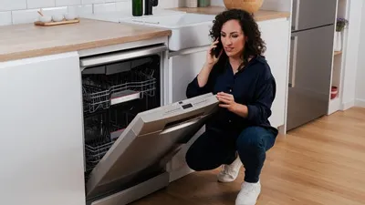 alt-Woman registering a dishwasher by phone in a bright kitchen.
