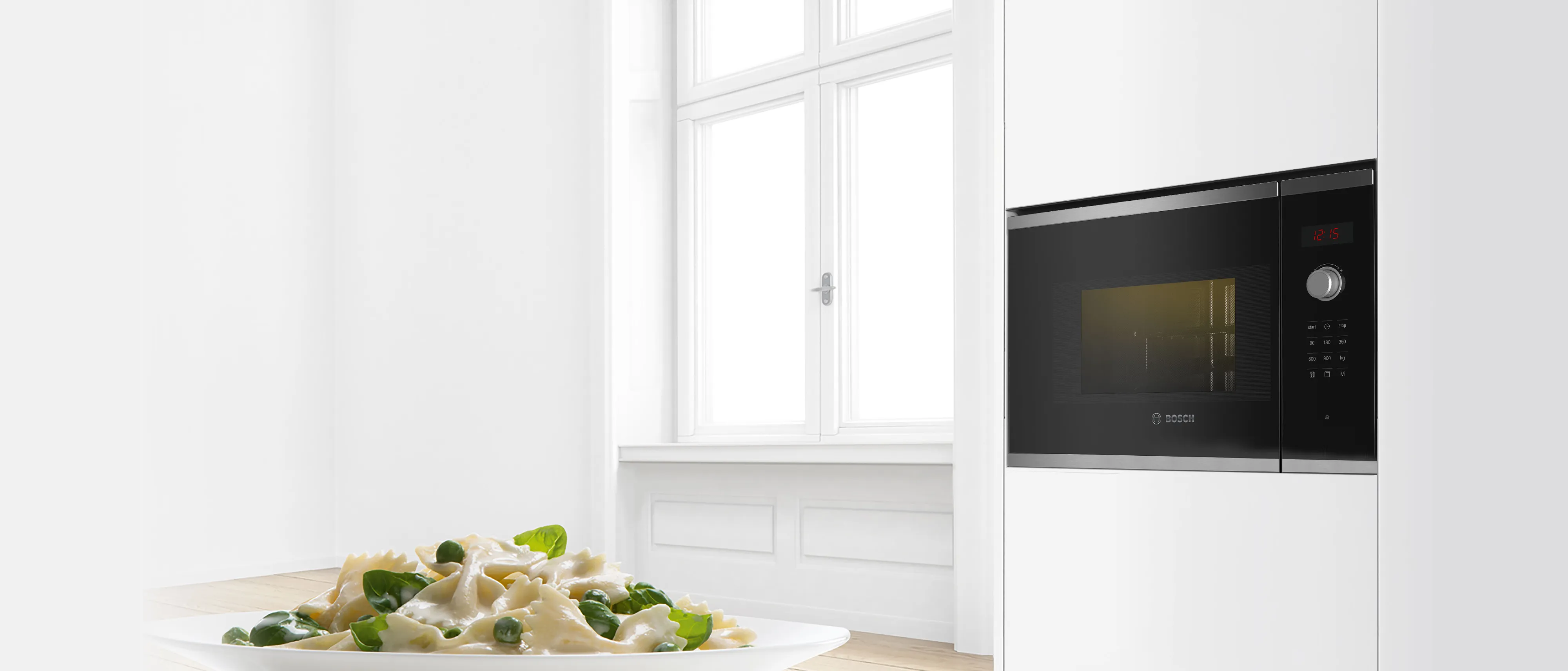 Built-in Bosch microwave seamlessly integrated on top of an oven into a modern white and wood kitchen design.