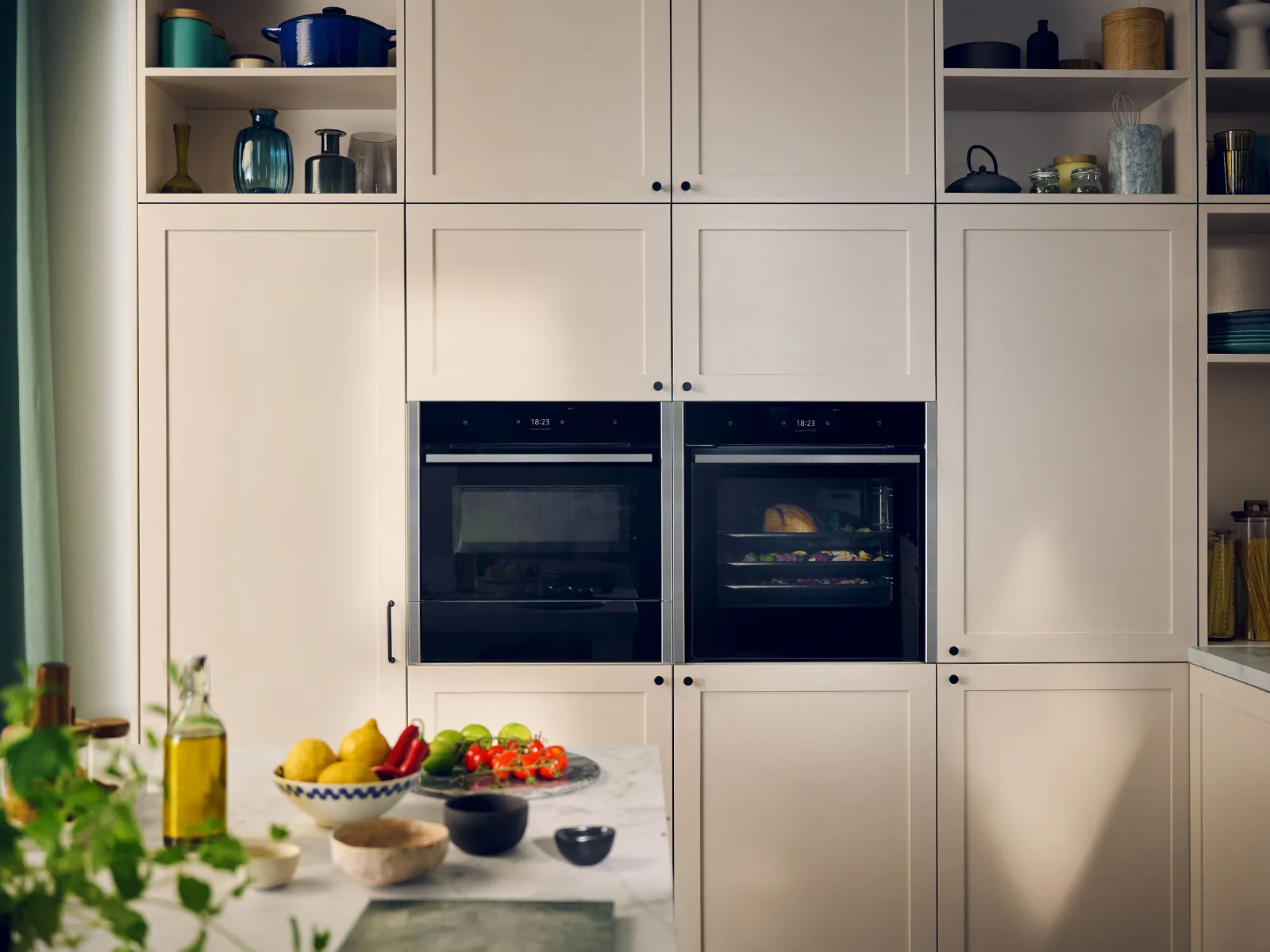 Two built-in slide and hide ovens within white kitchen cabinetry, next to a marble worktop.