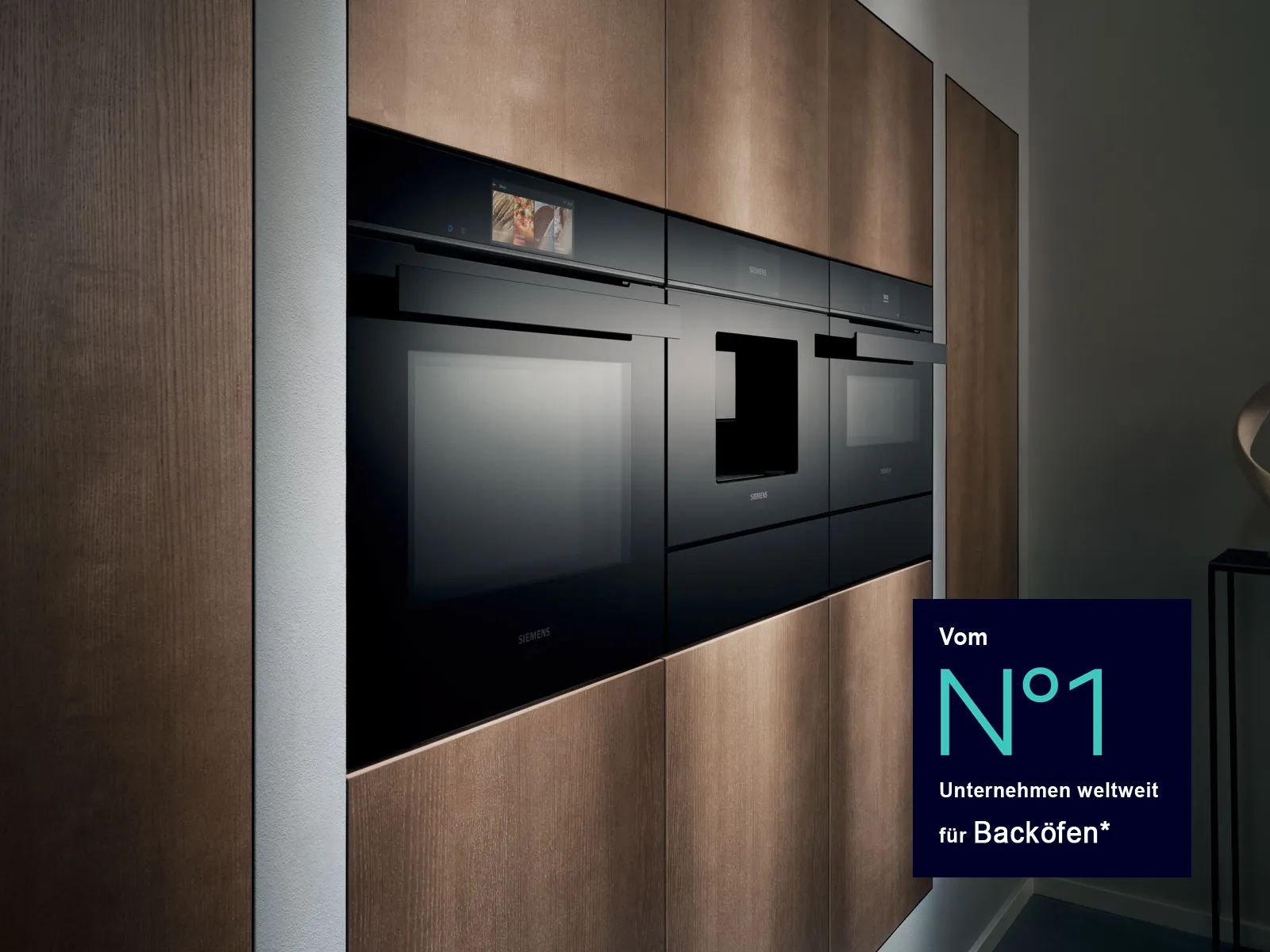 Moderne Einbauküche mit schwarzen Siemens Backöfen und integrierten Geräten in dunkler Holzfront. Unten rechts ein blaues Badge mit dem Hinweis: „Vom Nr. 1 Unternehmen weltweit für Backöfen*“.
