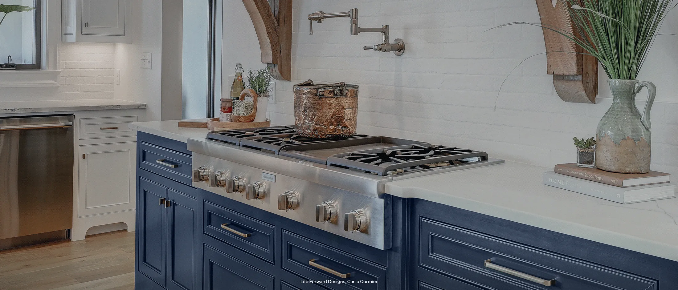 Modern kitchen featuring a sleek gas stove with stainless steel knobs, set in a blue island with white countertops and white brick backsplash.