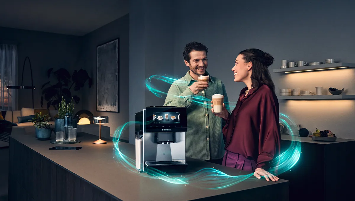 A couple standing at the kitchen counter next to the Siemens EQ900 iAroma espresso machine drinking Latte macchiato and Cappuccino.