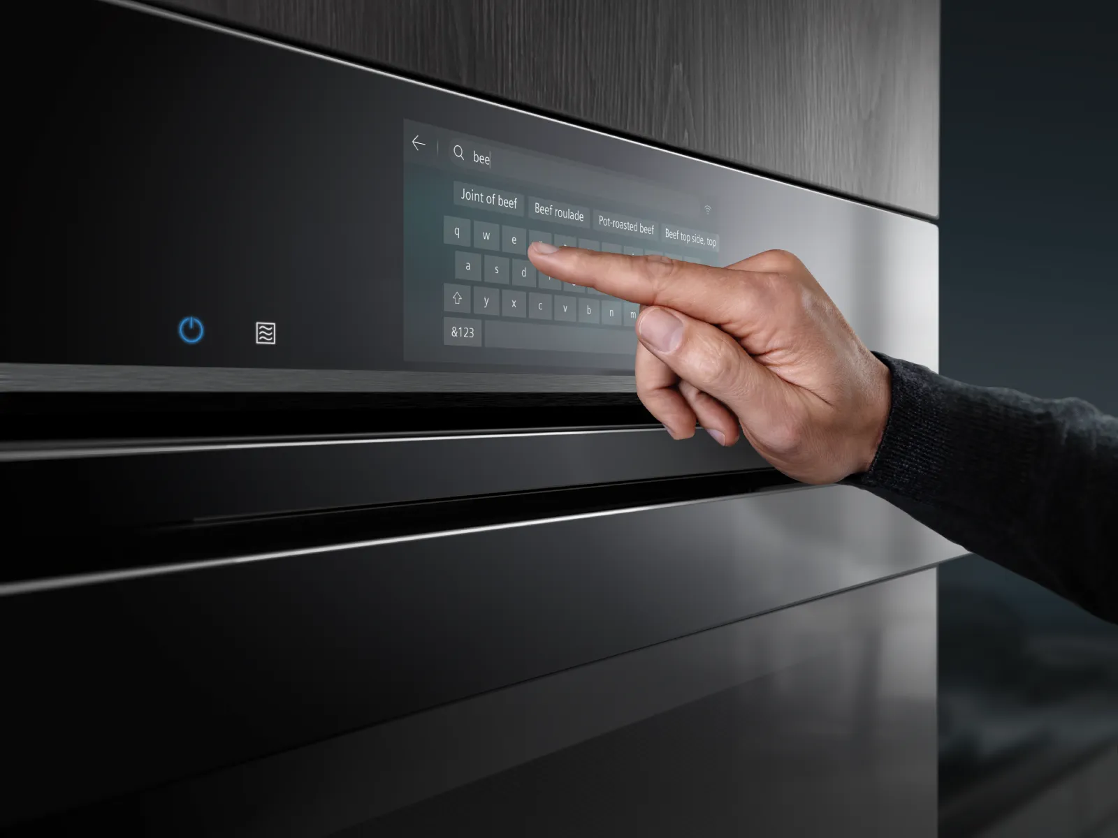 Hand touching a modern oven's digital touchscreen, typing "bee" and displaying cooking options for beef dishes.