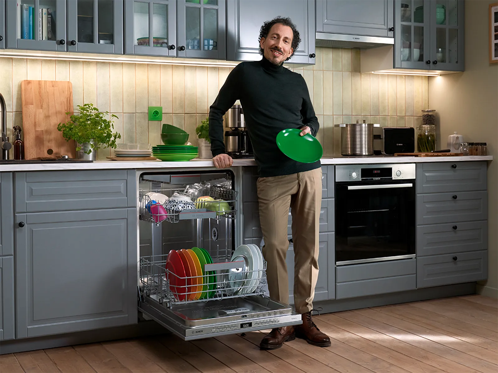 Person standing in a modern kitchen next to an open dishwasher holding a green plate.