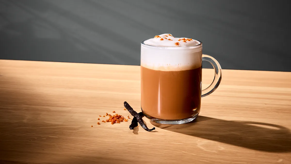 A Vanilla Latte Macchiato on a wooden table with cinnamon sticks next to it