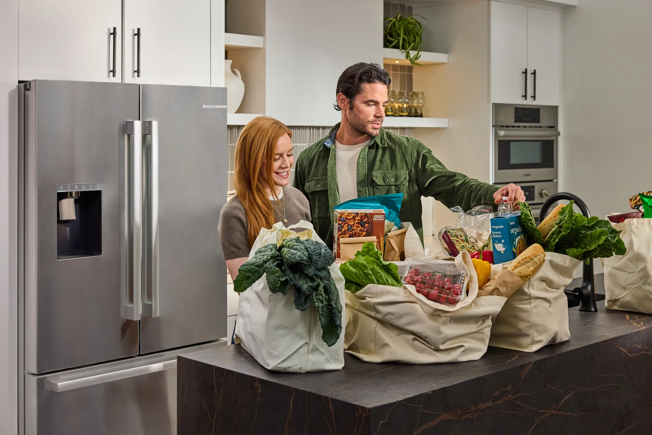 Family in kitchen with groceries on countertop next to a Stainless steel Bosch refrigerator