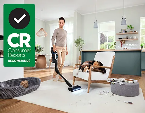 Badge «Recommandé par Consumer Reports» avec une femme passant l'aspirateur pour nettoyer le désordre dans le salon.