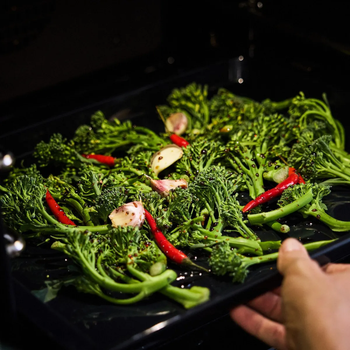 Person putting oven tray with veg on into oven