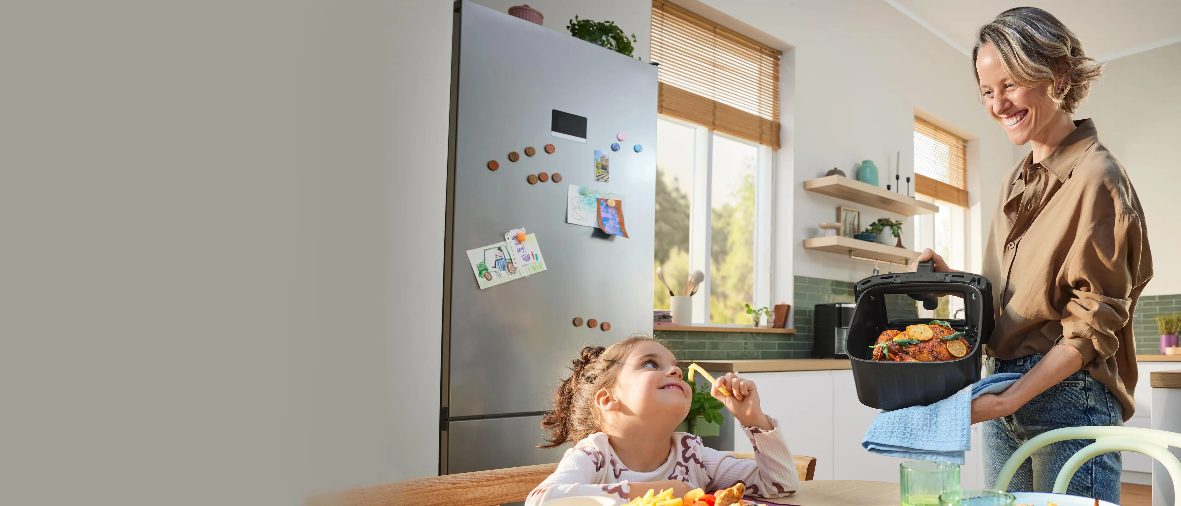 Kobieta i dziecko w kuchni air fryer na blacie w kuchni, obok potrawy na talerzach
