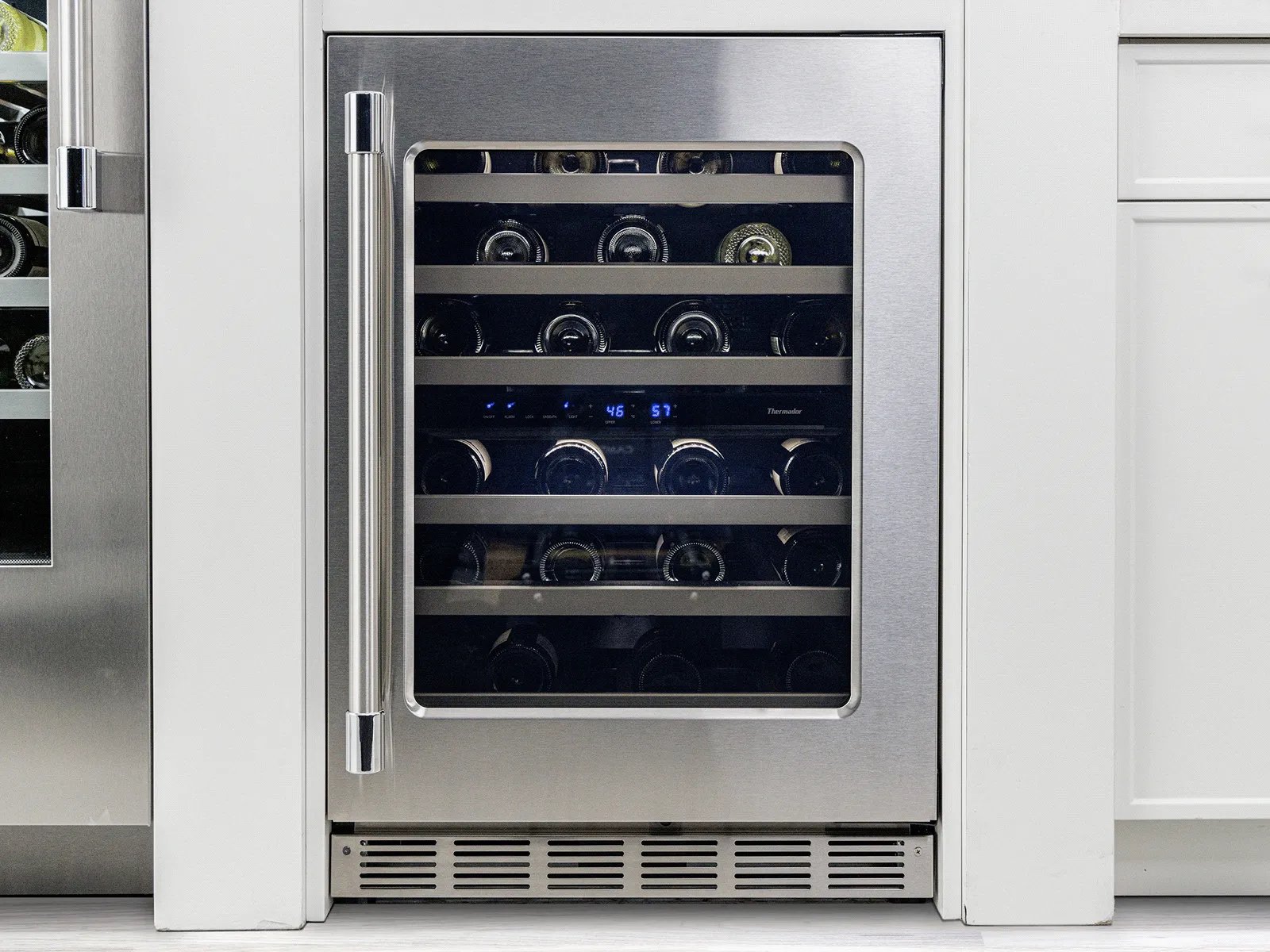 Built-in stainless steel wine cooler with glass door, holding multiple wine bottles inside a modern white kitchen.