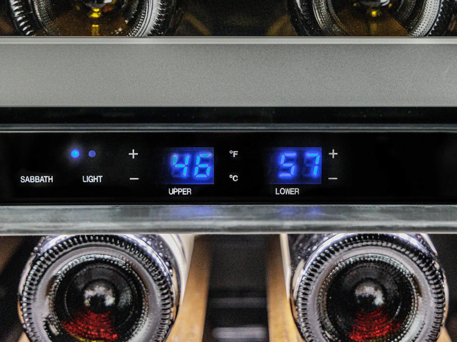 Close-up of a sleek black wine cooler displaying temperature controls and illuminated bottles inside.