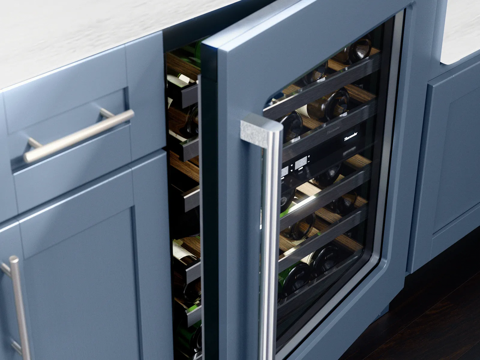 Under-counter wine refrigerator with a glass door ajar, showing horizontal bottles on wooden racks inside blue shaker-style kitchen cabinets with a stainless steel handle and dark hardwood floor.