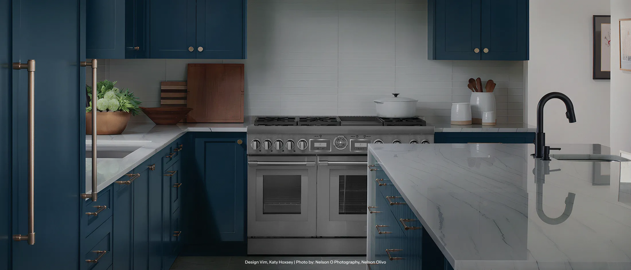 Modern kitchen with blue cabinets, white marble countertops, a large stove, and a sleek black faucet under bright lighting.