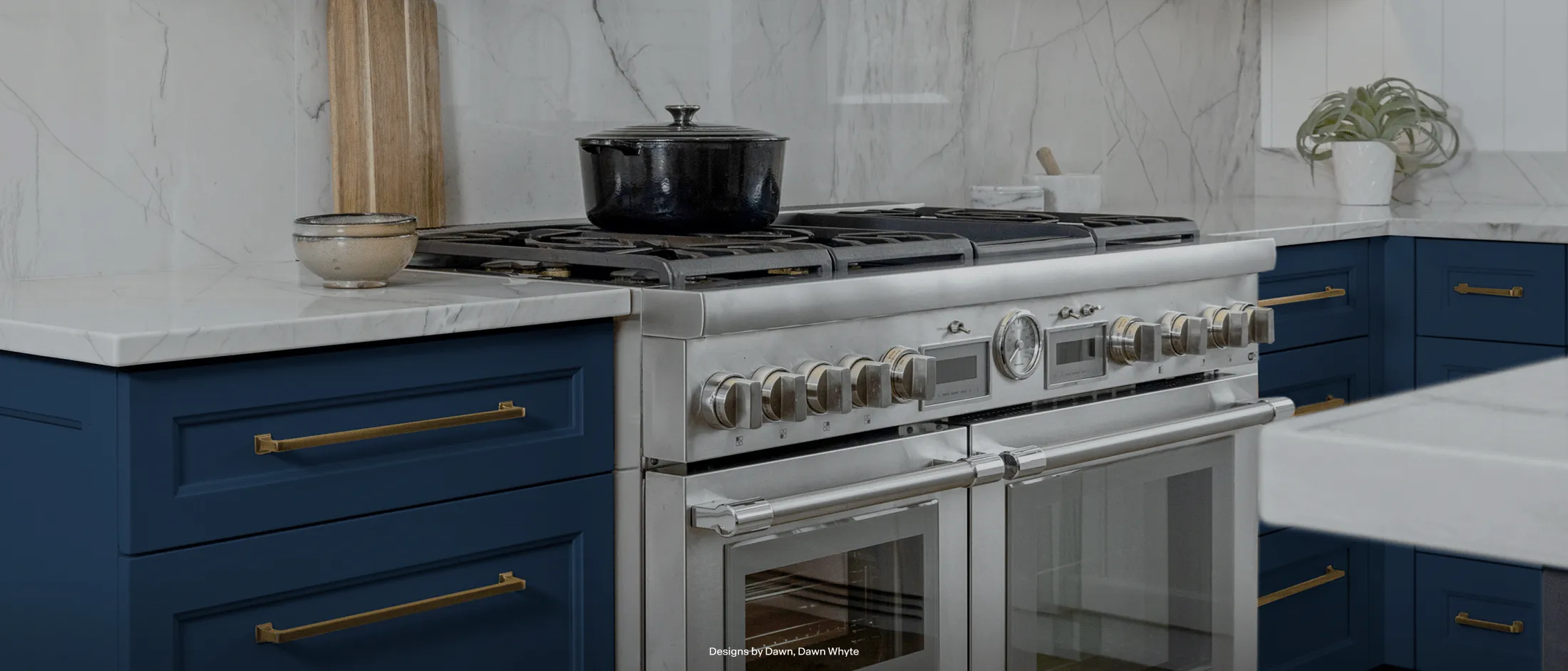 Modern kitchen featuring a stainless steel gas stove with a black pot, blue cabinets, white marble countertops, and brass handles.