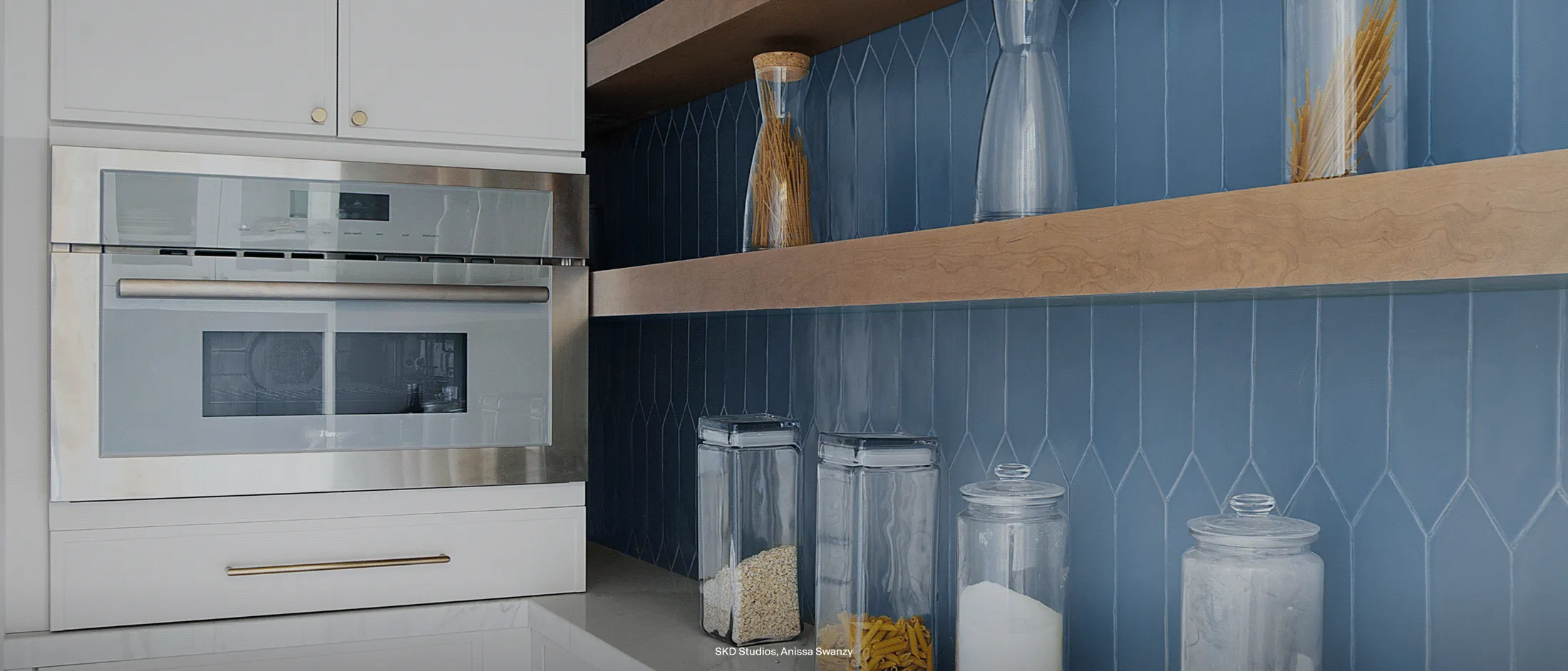 Modern kitchen with a built-in stainless steel oven and blue tiled backsplash.