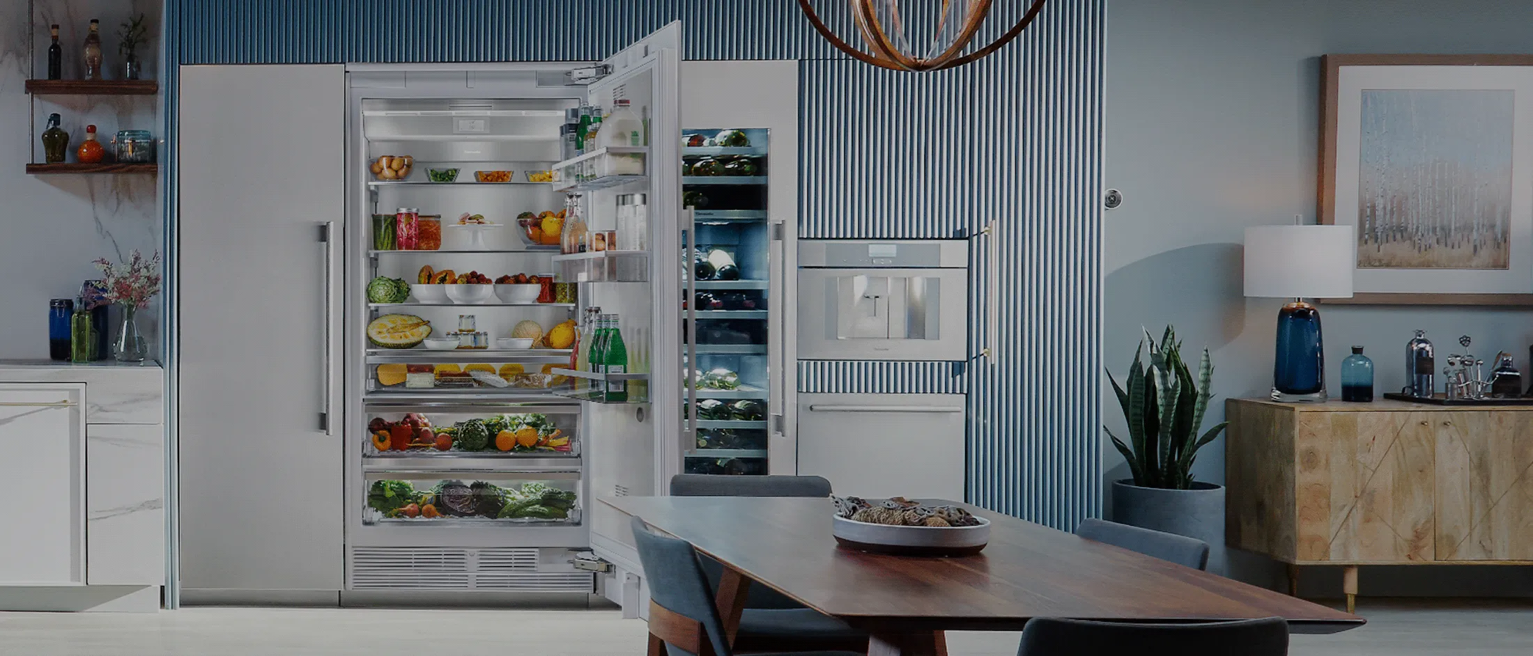 Modern open-concept kitchen and dining area with marble island, blue cabinets, white appliances, and stylish industrial lighting.