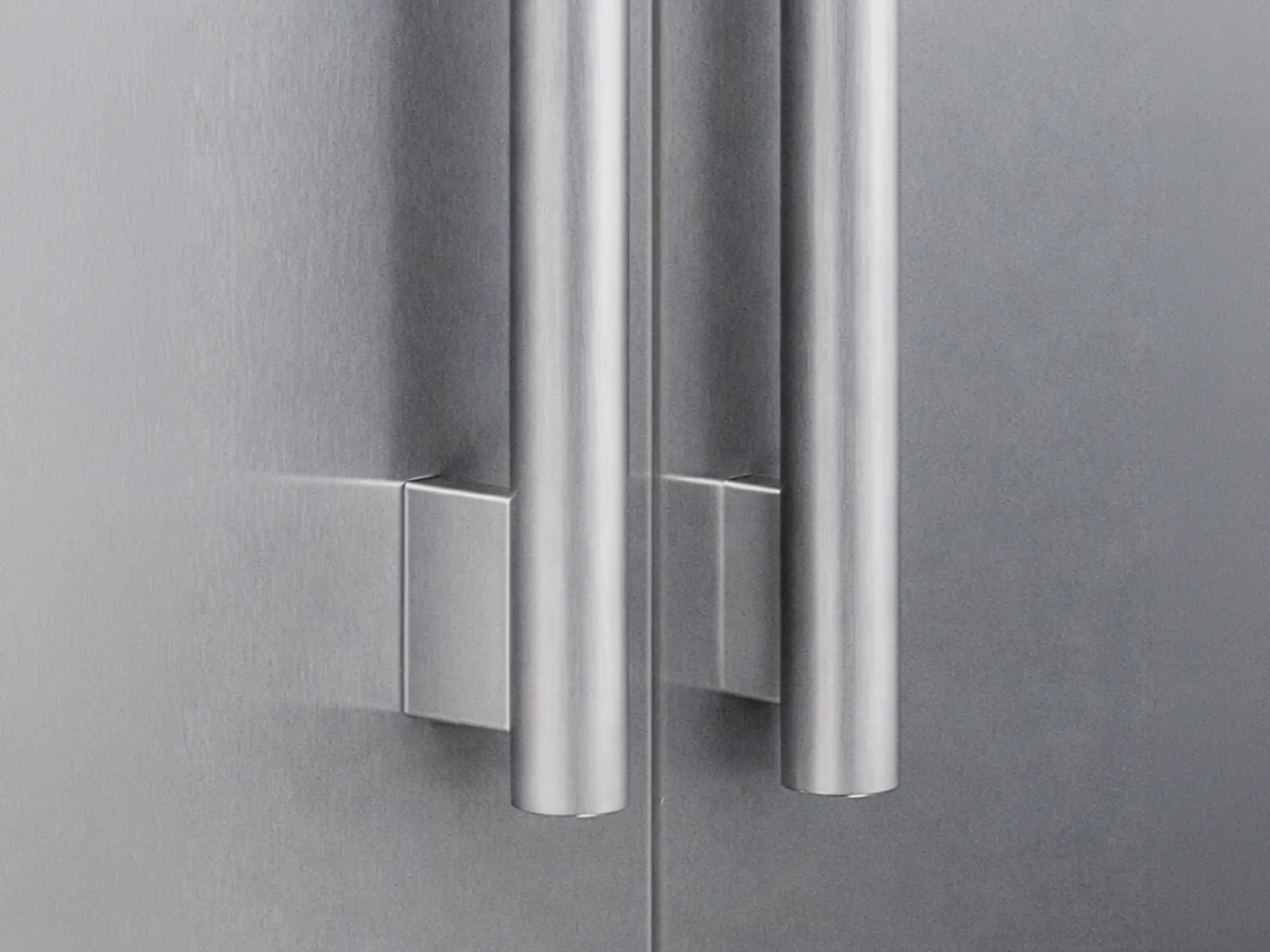 Close-up of two sleek stainless steel refrigerator door handles on a matte silver surface.