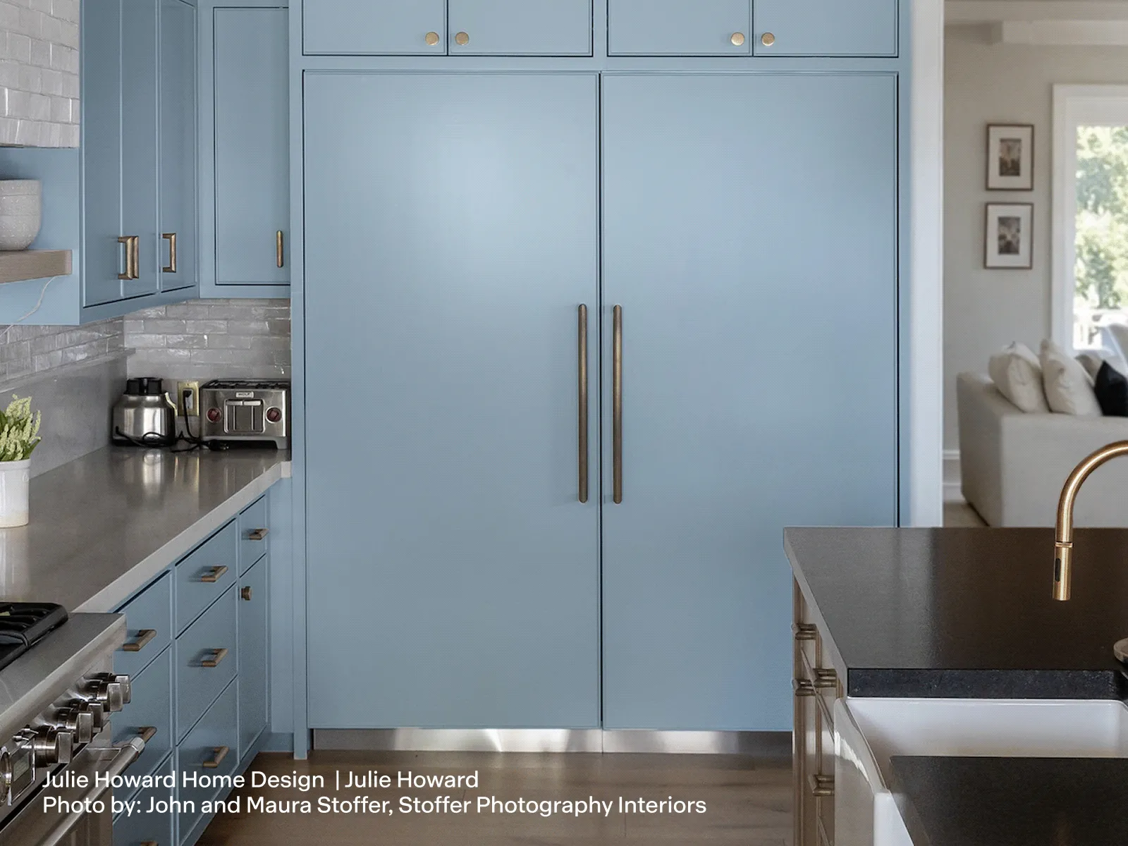 Modern kitchen with light blue cabinets, wooden beam ceiling, large island with black countertop, and stainless steel appliances.