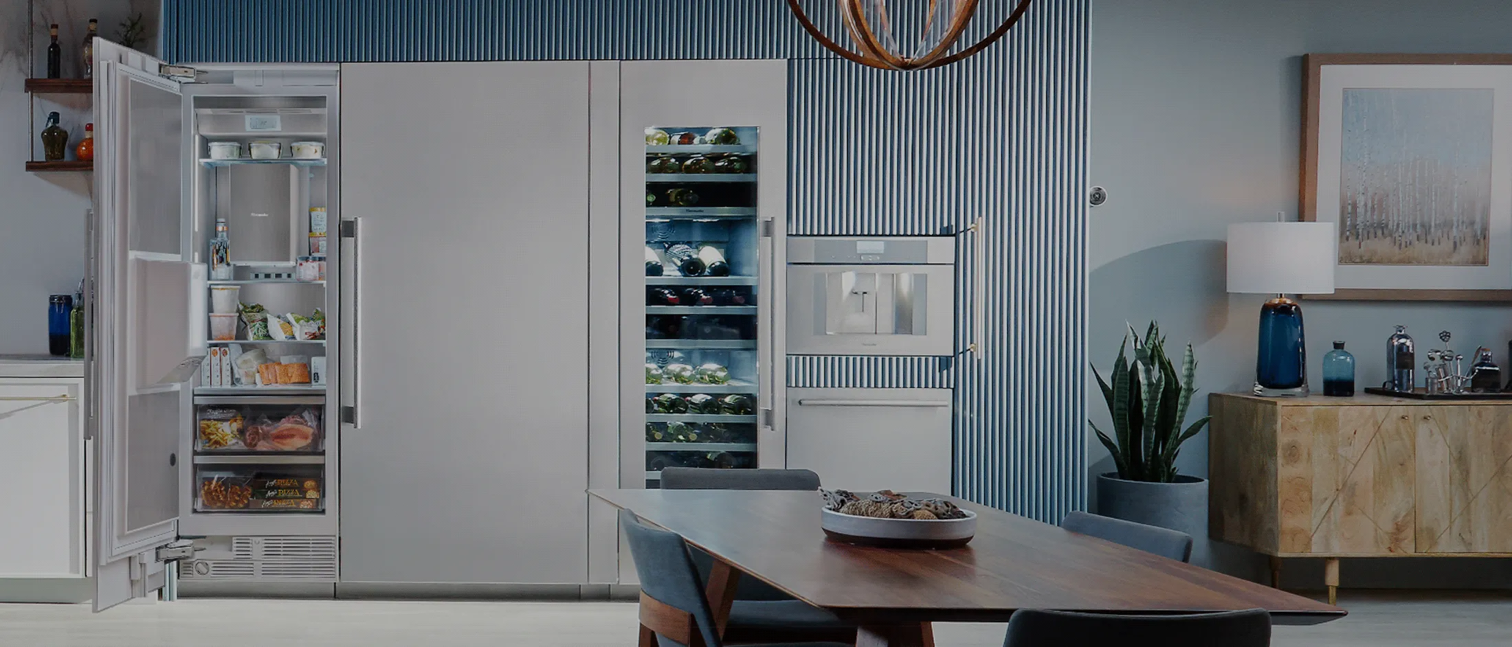 Modern open-concept kitchen and dining area with marble island, white cabinetry, blue accent wall, and wooden dining table with chairs.