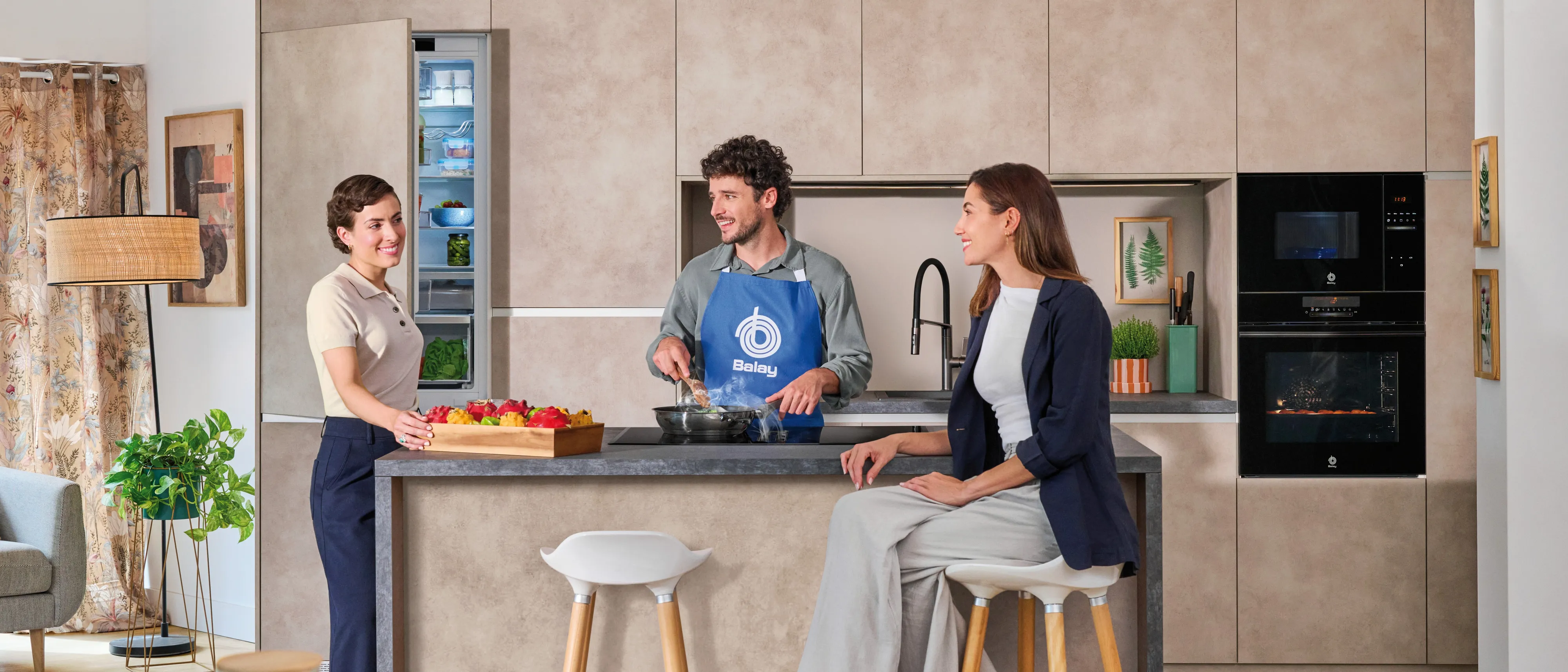 Três pessoas em uma cozinha moderna, preparando comida e conversando.
